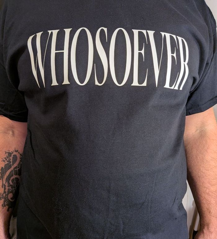 A black WHOSOEVER T-shirt being worn, photographed from the chest down.